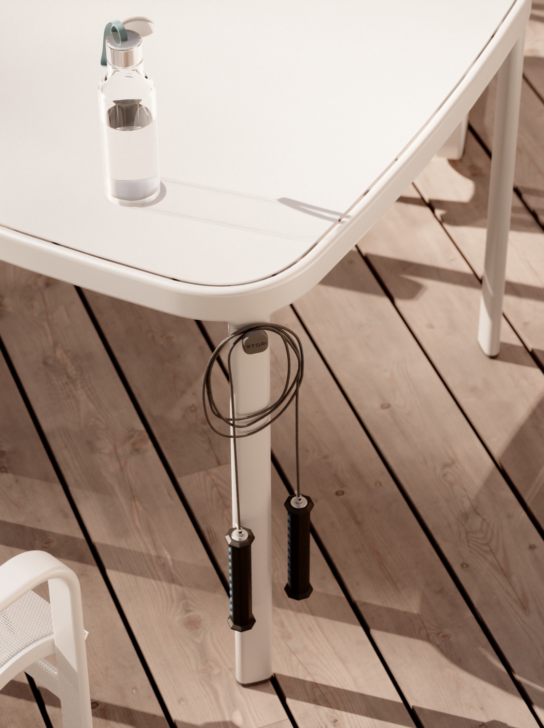 A clear water bottle sits on a white outdoor table, with a jump rope neatly wrapped around one leg. The scene unfolds on a wooden deck, with a classic sling chair from the Sequel collection enhancing the clean, minimalist setting crafted by Stori Modern.