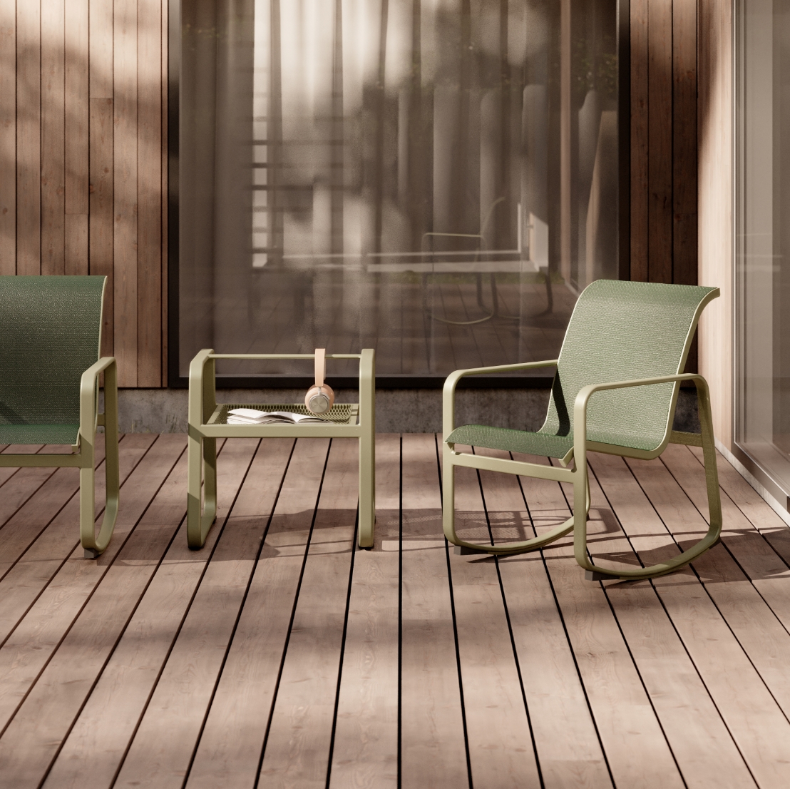 A serene patio setting features a light green rocking chair and matching armchair from the Sequel collection, paired with a low table holding a glass and candle. The wooden decking and soft shadows from surrounding plants create a tranquil outdoor environment reminiscent of Stori Moderns elegance.